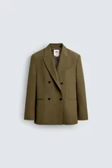 Blazer color verde oliva de corte regular, confeccionada en tejido con lana. Presenta cuello con solapas de pico, manga larga con puños abotonados, bolsillo de vivo en pecho, bolsillos de doble vivo en cadera, bolsillo interior y aberturas en la espalda. Cierre frontal cruzado con doble botonadura.