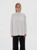 Buzo tejido color blanco, con cuello subido tipo polera, diseño oversized y largo con pequeños cortes laterales.