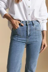 Jean de corte recto y tiro medio, color gris oscuro con efecto lavado. Presenta apliques de tachas metálicas pequeñas en la zona de los bolsillos delanteros.