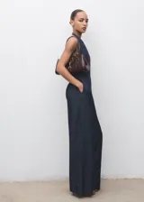 Mono largo de denim azul oscuro, sin mangas, con cuello halter y escote en la espalda. Presenta un corte recto y holgado en las piernas.