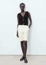 Chaleco negro de punto fino, sin mangas, con tirantes anchos, diseño recto, cuello de pico y cierre delantero con botones.