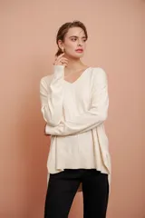 Buzo color crema de tejido de punto, con escote en V y corte asimétrico, más largo en la parte trasera.