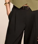 Pantalón wide leg negro de poliéster y elastano, con trabillas en la cintura, cinturón con hebilla y pliegues. Estilo sastrero.