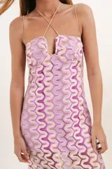 Vestido largo de crochet color lila y beige con breteles finos cruzados en la espalda y escote en V. El forro es corto, dejando ver las transparencias del tejido.