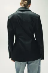 Blazer entallada negra de efecto piel, con cuello solapa y manga larga. Tiene bolsillos de plastrón en el delantero, costuras marcadas y forro interior combinado a tono. El cierre es frontal con botón interior y exterior.