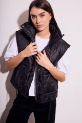 Chaleco negro acolchado con cierre frontal y cuello alto. Diseño reversible con cordones ajustables en la cintura.