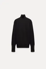 Jersey negro de punto liso con cuello alto, manga larga y detalle de botones dorados en los puños.