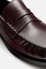 Mocasín de cuero color borgoña, con antifaz y suela negra en contraste.