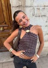 Top marrón con estampado de lunares blancos, cuello halter con lazo y detalle de logo dorado.