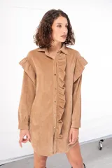 Camisa larga color beige de pana fina con cuello camisero, cierre frontal con botones y mangas largas con puños abotonados. Presenta volados en los hombros y a lo largo del cierre frontal.