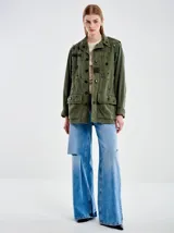 Chaqueta militar verde oliva de algodón con cuello camisero, cierre frontal con botones y cuatro bolsillos delanteros con solapa. Decorada con apliques metálicos y parches de tela.