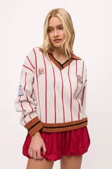 Sweater de punto color crudo con rayas verticales rojas, cuello polo marrón con borde negro, puños y ruedo acanalados en marrón y negro.