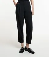 Pantalón negro de corte carrot, con pliegues delanteros, abotonado frontal y detalle en el bajo.