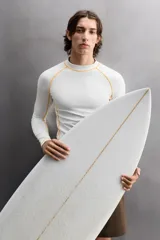 Camiseta de surf compresiva slim fit confeccionada en tejido técnico muy elástico y ligero. Con factor de protección ultravioleta 40+, cuello subido, manga larga, costuras planas y acabados combinados a contraste.
