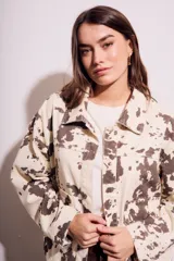 Campera de algodón color crema con estampado de manchas marrones tipo vaca, corte al cuerpo, con cuello clásico, cierre frontal con botones y bolsillos de parche en el pecho.