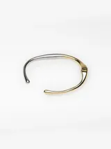 Pulsera rígida de diseño minimalista con acabado bicolor en tonos dorado y plateado. Presenta una estructura metálica con apertura de bisagra y extremos abiertos redondeados.