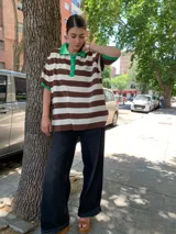 Remera oversize a rayas horizontales marrones y blancas, con cuello polo y mangas cortas con ribete verde.