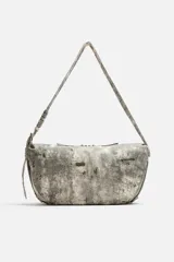 Bolso de hombro color gris con efecto desgastado, fabricado en tejido de algodón. Tiene un compartimento principal con cierre de cremallera, un bolsillo interior con cremallera y asa de hombro ajustable.