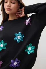 Sweater negro con aplicaciones de flores brillantes en tonos verdes y morados, de corte holgado.