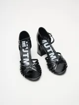 Sandalias negras de charol con tiras cruzadas en el empeine, pulsera con hebilla al tobillo y tacón cuadrado.