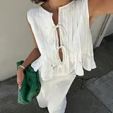 Conjunto de top y falda color crema, confeccionado en lino. El top es sin mangas, con detalle de lazos en el escote y volados en el ruedo. La falda es larga y de corte recto.