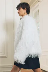 Chaqueta de pelo sintético color blanco, de cuello redondo y manga larga. Tiene bolsillos delanteros, forro interior y cierre frontal con ganchos metálicos forrados.