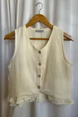 Blusa color crema de muselina 100% algodón, con escote en V, sin mangas, con botones al frente y volados en el ruedo.