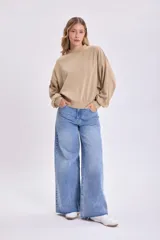 Buzo color beige de corte holgado, con cuello redondo y mangas abullonadas.