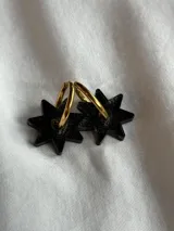 Par de aros colgantes con forma de estrella negra y aro dorado.