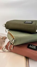 Billetera corta con cierre alrededor y tapa, confeccionada en tela capitoneada. Incluye varias reparticiones con tarjeteros y bolsillos internos, y una correa de mano desmontable. Disponible en negro, rojo y dorado.