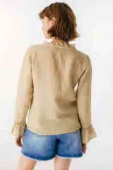 Blusa blanca de lino con botones de nácar, volados en el escote y mangas largas con puños acampanados. Corte recto y holgado.