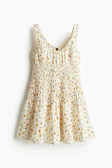 Vestido corto blanco con estampado de naranjas, breteles anchos y escote en U. Presenta frunces en el busto y falda con volados.