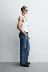 Pantalón de jean celeste de corte flare, con tiro medio, cinco bolsillos, cierre frontal con cremallera y botón, y bajo con acabado irregular.