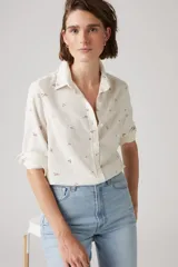 Camisa de lino color blanco hueso con estampado floral en tonos marrones. Tiene cuello clásico, cierre frontal con botones y mangas largas con puños abotonados.