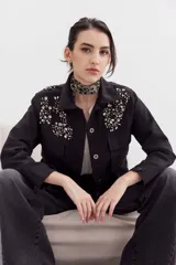 Campera negra de gabardina de algodón con corte holgado y cordón de ajuste en la cintura. Presenta bordados a mano con piedras en la parte superior.