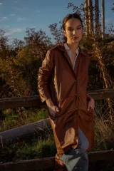 Gabardina marrón de cuero ovino italiano, con cuello camisero, cierre frontal con botones, mangas largas y corte recto.