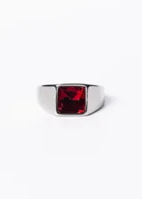 Anillo plateado de acero quirúrgico con piedra roja cuadrada en el centro.