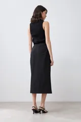 Falda midi negra de corte recto, con tajo lateral y cinturón con hebilla metálica.