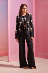 Chaqueta negra de punto jacquard con lúrex y forro interior, corte entallado y mangas acampanadas con abertura. Presenta flores blancas y doradas bordadas a mano.