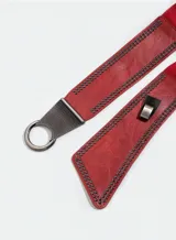 Cinto ancho de cuero sintético color burdeos, con elástico en la parte trasera y tachas pequeñas plateadas en los bordes. Presenta hebilla metálica plateada con forma circular.