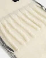 Bufanda tejida color crema con flecos en los extremos y etiqueta de cuero sintético negra.