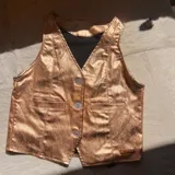 Chaleco dorado brillante con cuello en V, cierre frontal con tres botones y dos bolsillos simulados.