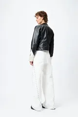 Pantalón de denim blanco con calce wide leg y ruedo desflecado. Presenta tachas metálicas a lo largo de los laterales.