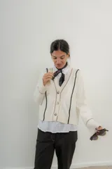 Saco color crema con cuello en V, cierre con botones, ribete negro y rojo en cuello, puños y borde inferior.