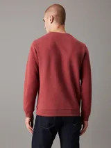 Buzo de felpa color ladrillo con cuello redondo, puños y bajo acanalados. Presenta un logo bordado de Calvin Klein Jeans en el pecho.