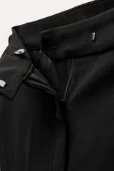 Pantalón negro de tiro alto con trabillas en la cintura, bolsillos delanteros y traseros, raya planchada en el frente, pierna recta y bajo acampanado.