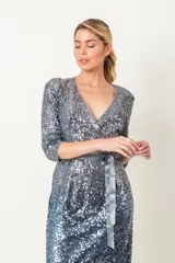 Vestido cruzado en paillette color plateado, con manga tres cuartos y falda con bordado degradé, complementado con lazo en gris plata.