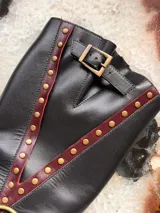 Botas de cuero negro con detalles en color borgoña, hebilla en la parte superior y arnés con aro metálico.