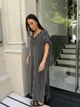 Vestido largo de tejido a rayas horizontales en tonos beige y blanco, con escote en V y mangas cortas tipo murciélago. Presenta tajos laterales en el ruedo.