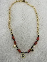 Collar corto con cadena dorada y dijes colgantes de coral, perlas y dijes dorados con detalles en negro.